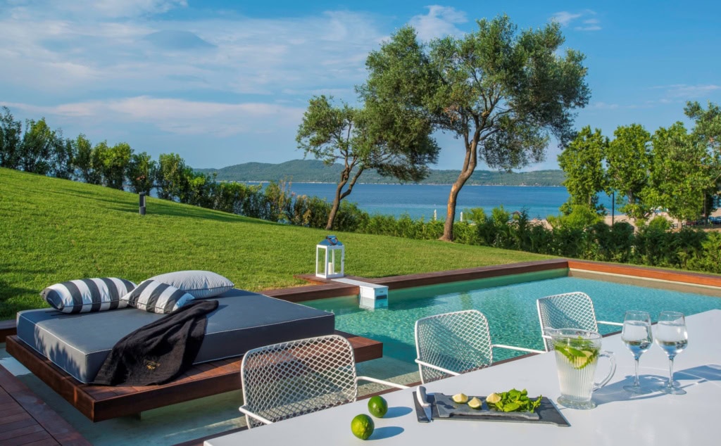 Aussenbereich des Avaton Luxury Beach Resort bei Chalkidiki; im Vordergrund ein weißer Tisch, dahinter eine elegante Liege und ein kleiner Pool.