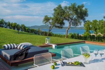 Aussenbereich des Avaton Luxury Beach Resort bei Chalkidiki; im Vordergrund ein weißer Tisch, dahinter eine elegante Liege und ein kleiner Pool.