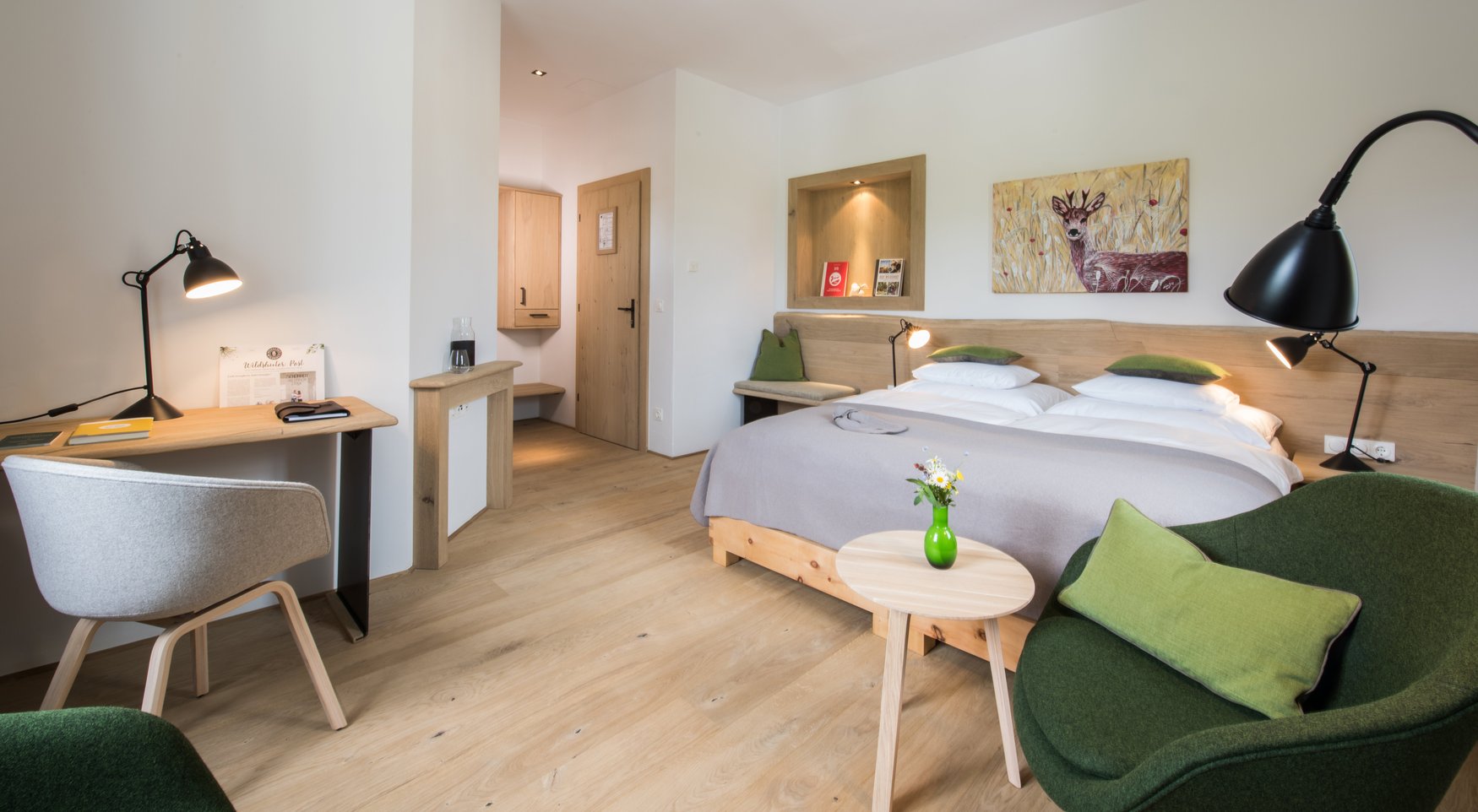 Doppelzimmer mit Holzbett, Schreibtisch, grünen Sesseln und einem Rehbild an der Wand.