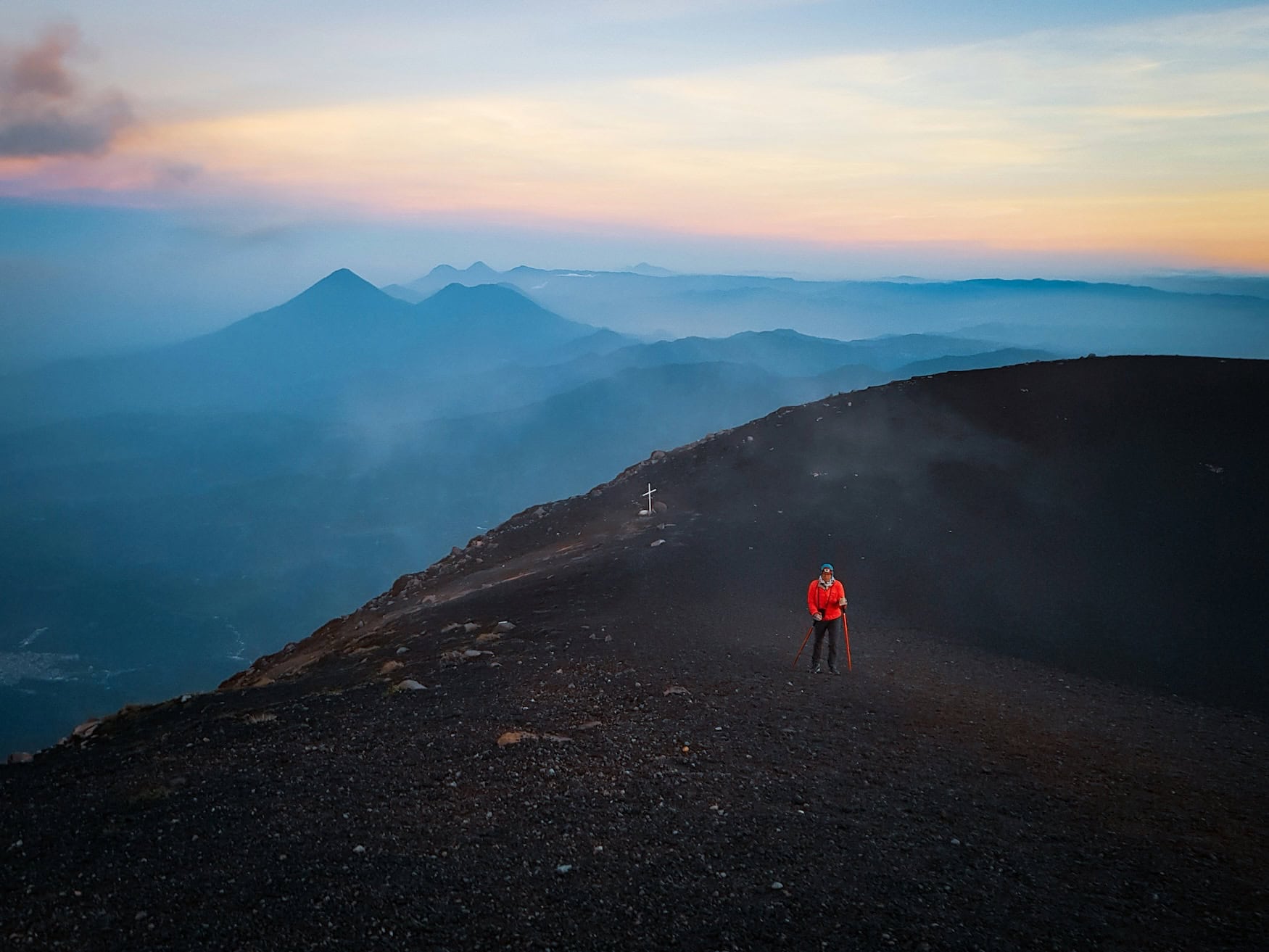 Am Gipfel eines Vulkans in Guatemala blickt eine wandernde Person bei Morgendämmerung über die Vulkankette.