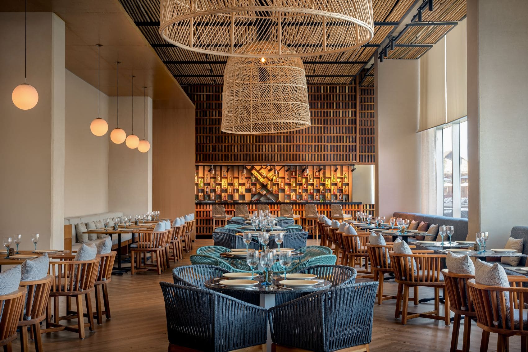 Restaurant im Mondrian Cancún mit Holzmöbeln, großen Flechtleuchten und Bar.