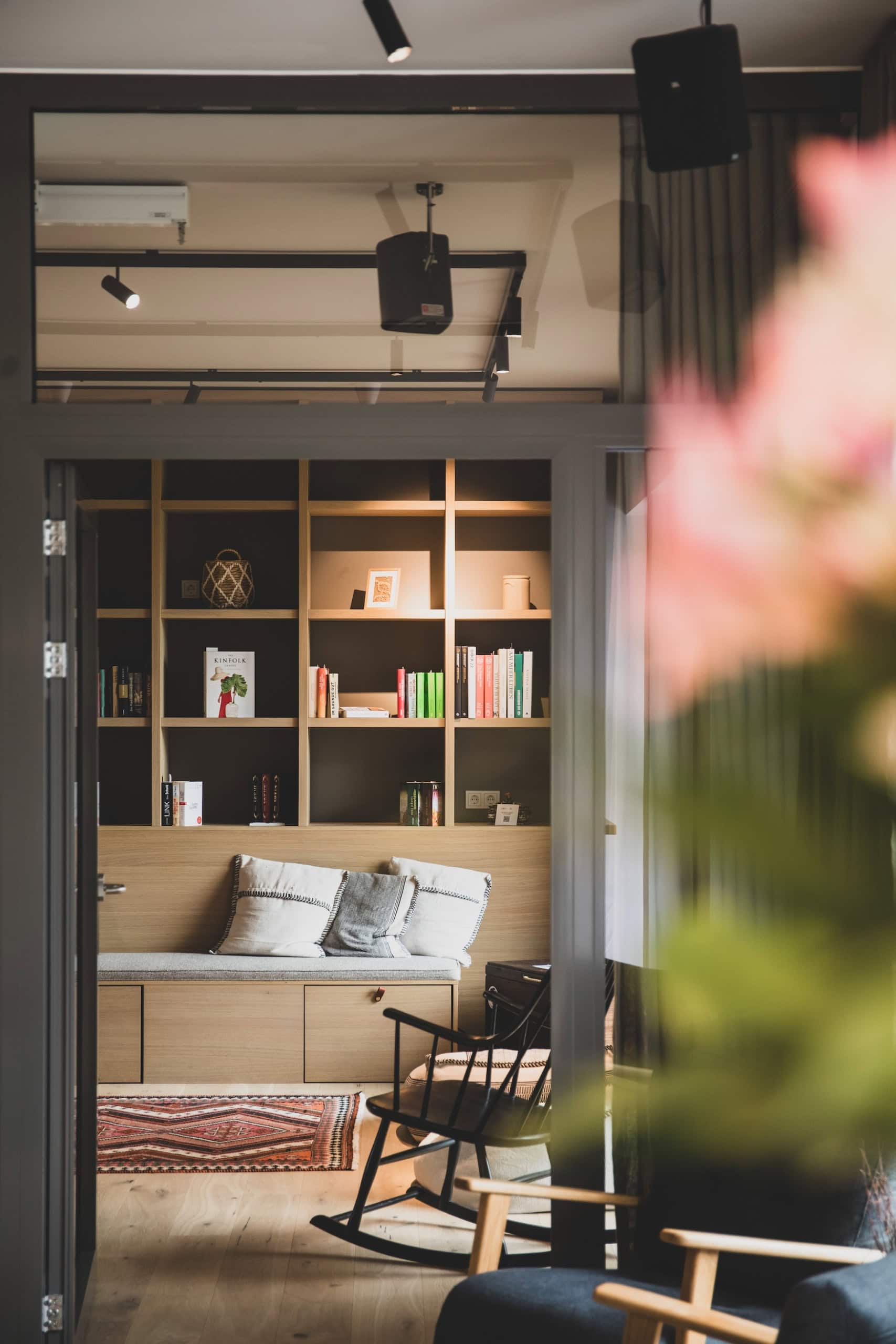 Gemütliche Leseecke im NOORD mit gefülltem Bücherregal, Sitzbank mit Kissen und einem schwarzen Schaukelstuhl.