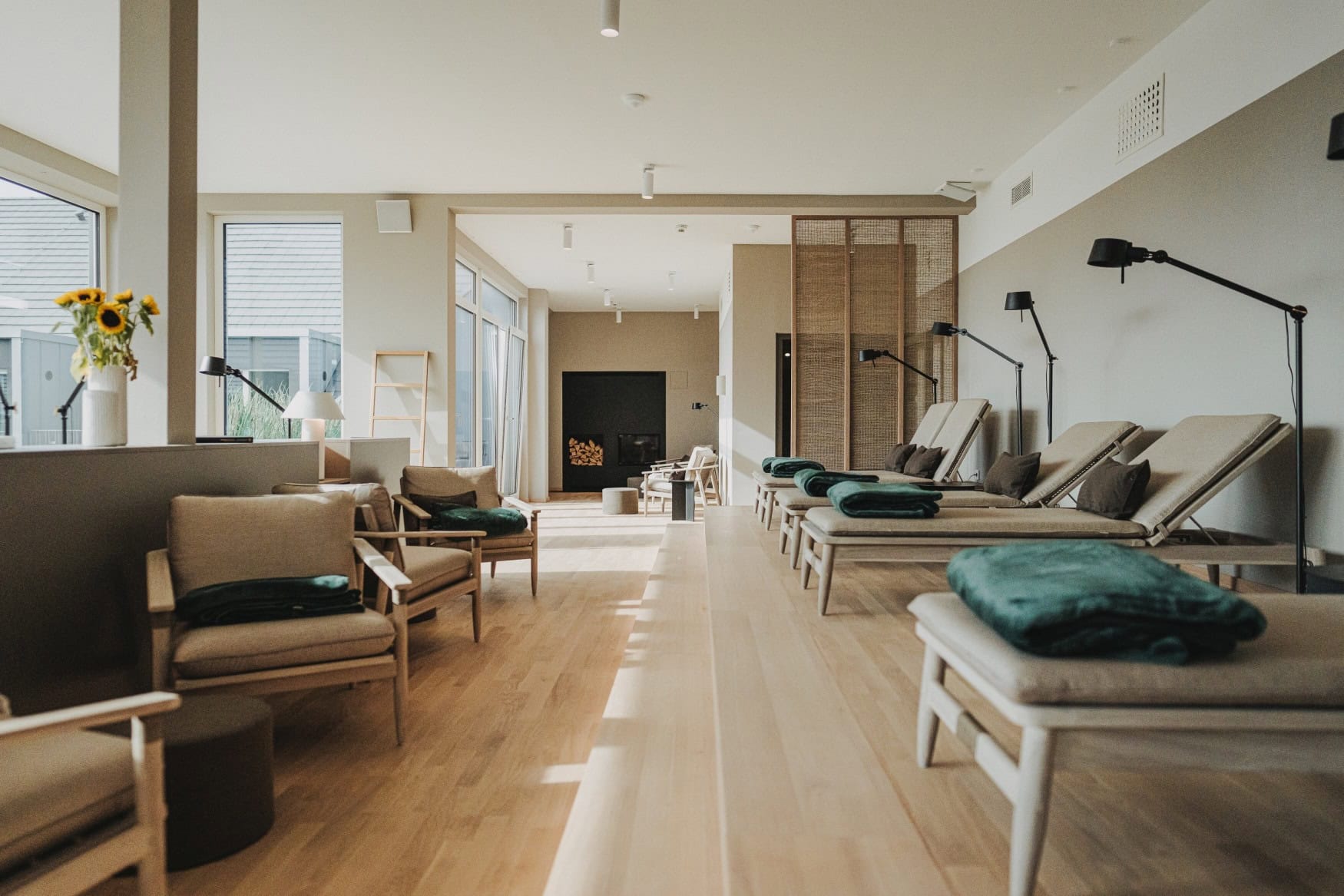 Ruheraum im Wellbee-Spa des NOORD mit hellen Holzliegen, grünen Decken und Sesseln vor einem Kamin.