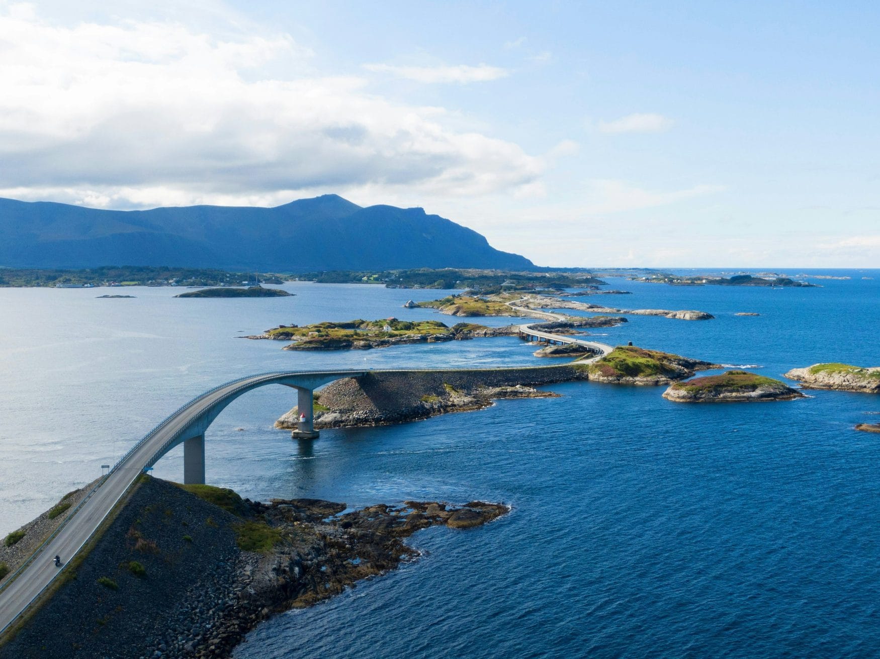 Die Atlantikstraße in Norwegen mit der geschwungenen Storseisundet-Brücke über das Meer, dahinter Schären und Berge