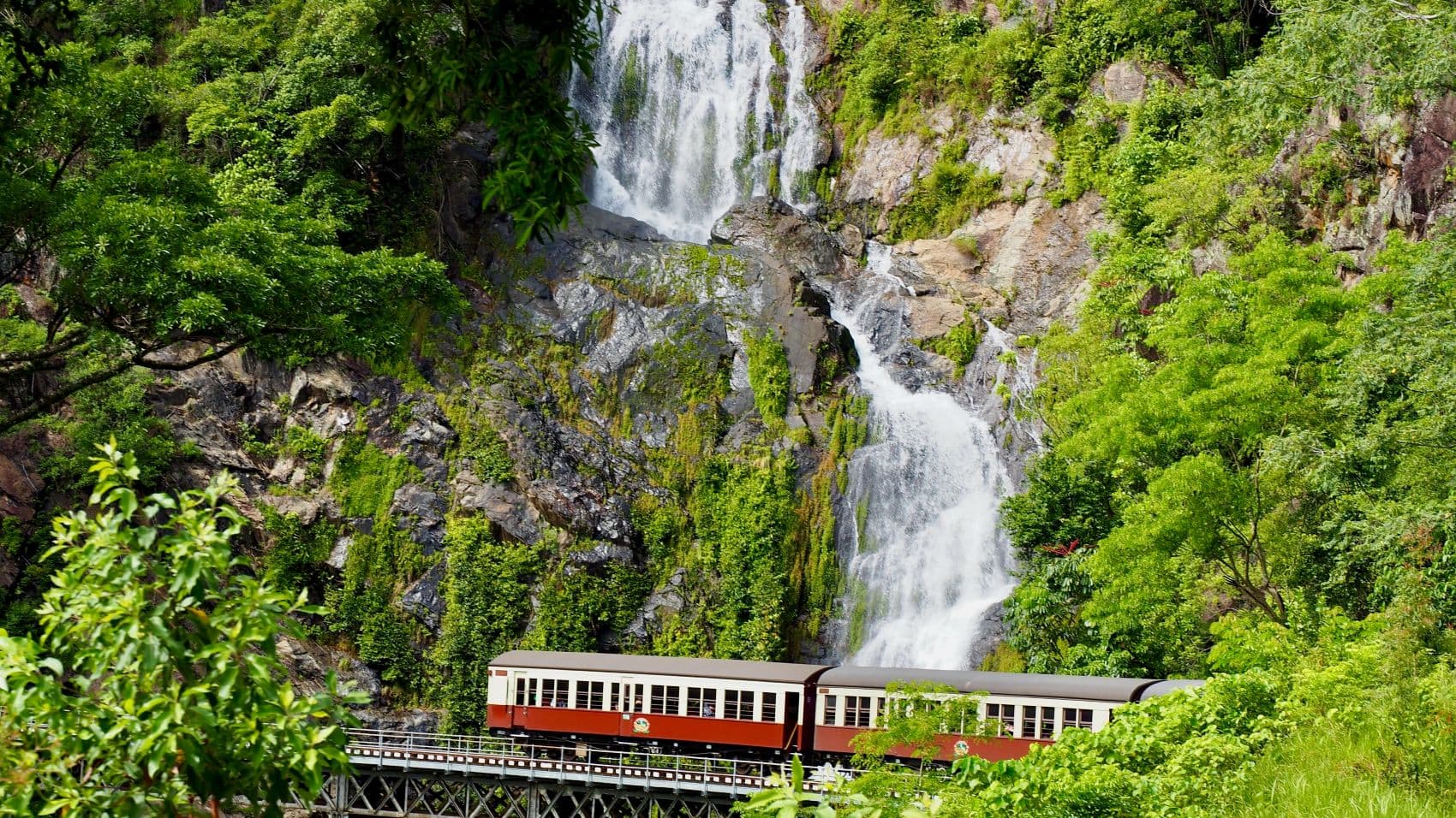 Kuranda Scenic Railway auf einer Brücke vor einem Wasserfall im tropischen Regenwald