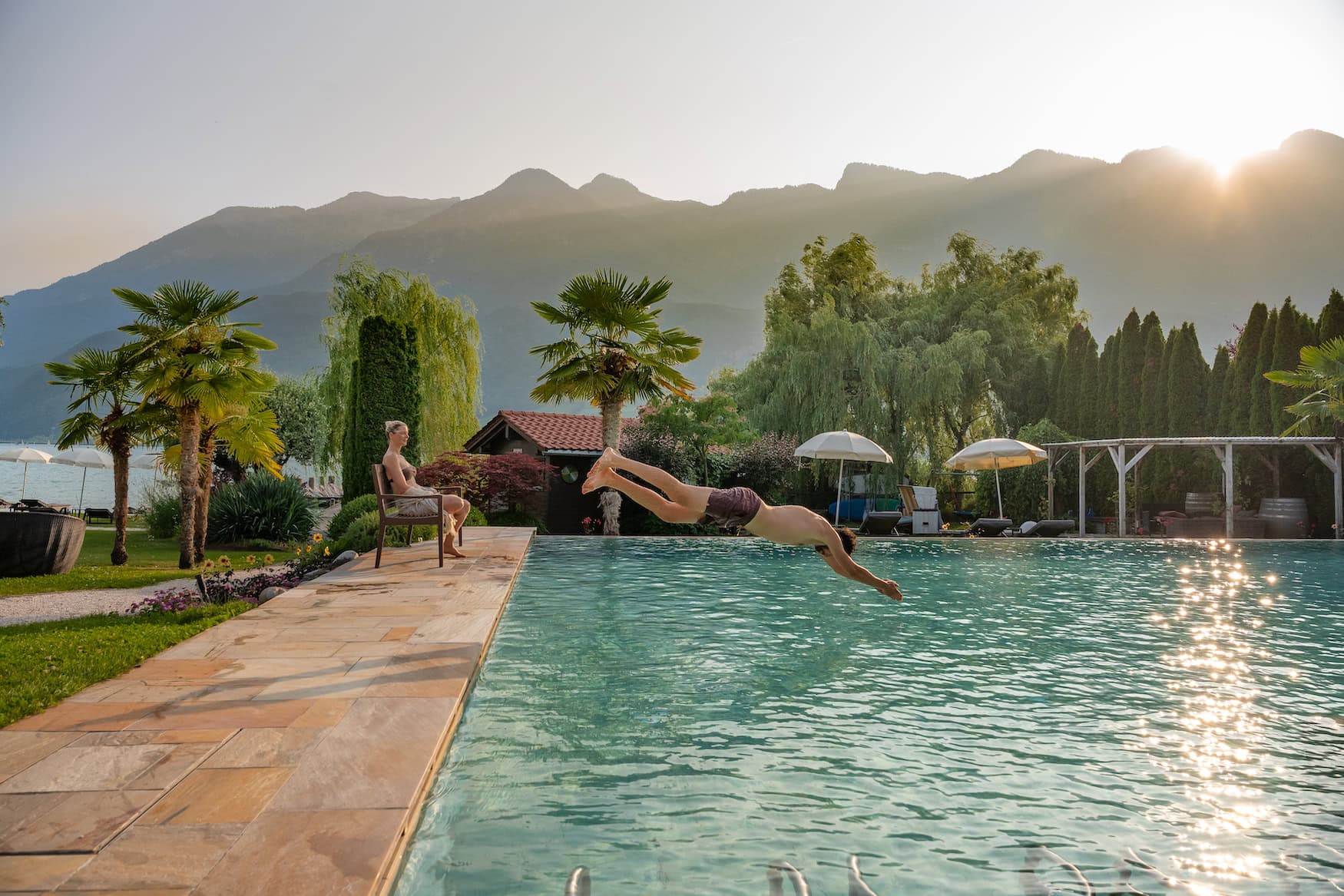 Gast springt in den Außenpool des Parc Hotel am See vor der Bergkulisse Südtirols.