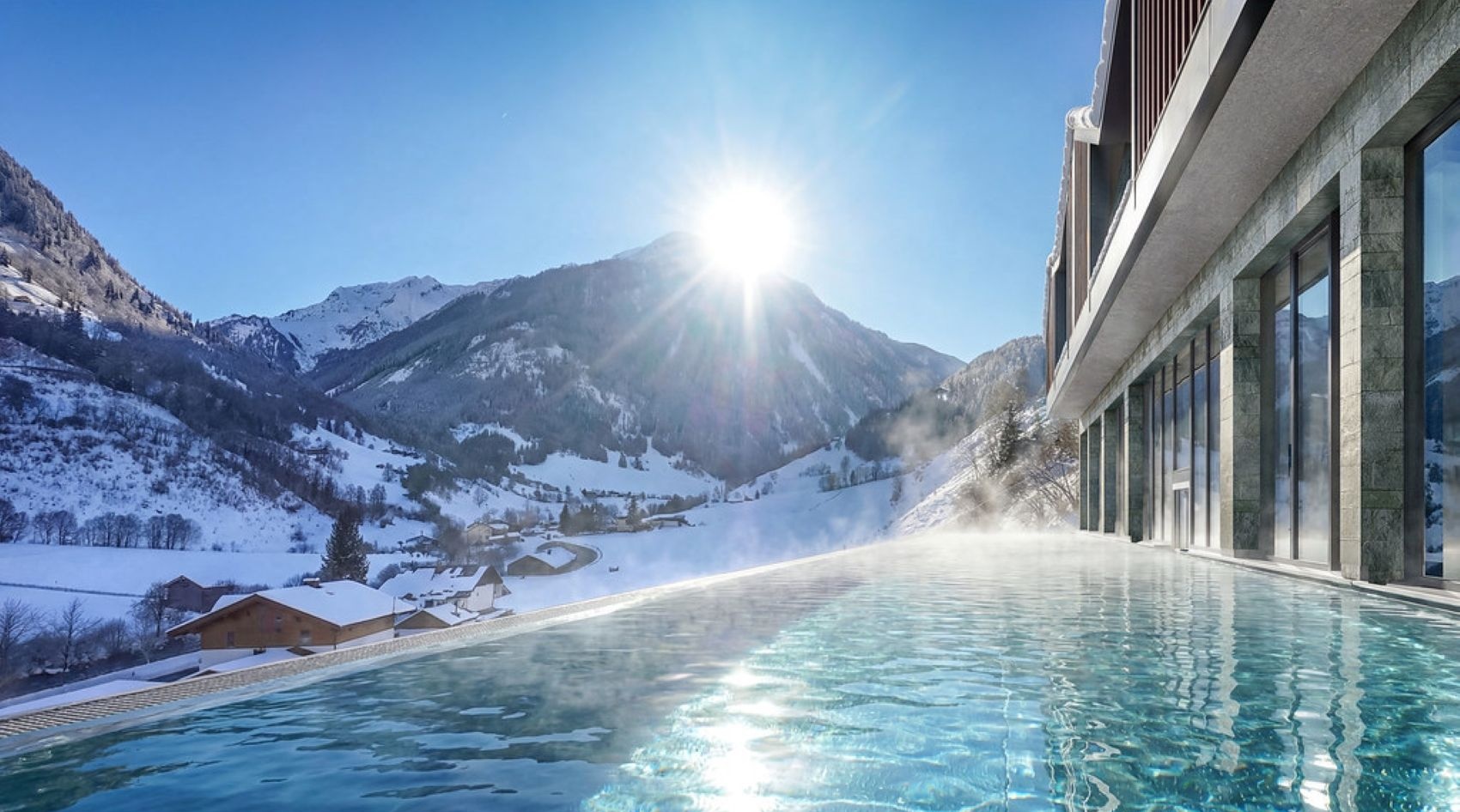 Infinitypool des glockna am Großglockner mit dampfendem Wasser, verschneiten Bergen und Wintersonne über dem Tal.