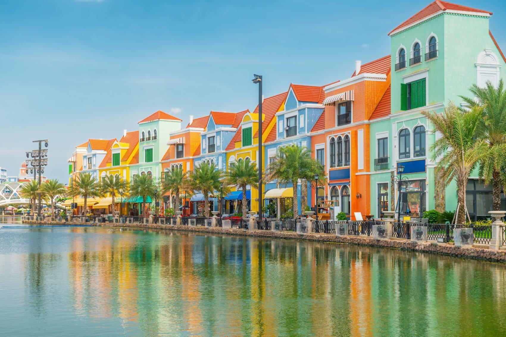 Bunte Gebäude im europäischen Stil am Venice Canal im Grand World auf der vietnamesischen Insel Phu Quoc, mit Palmen und Spiegelungen im Wasser.