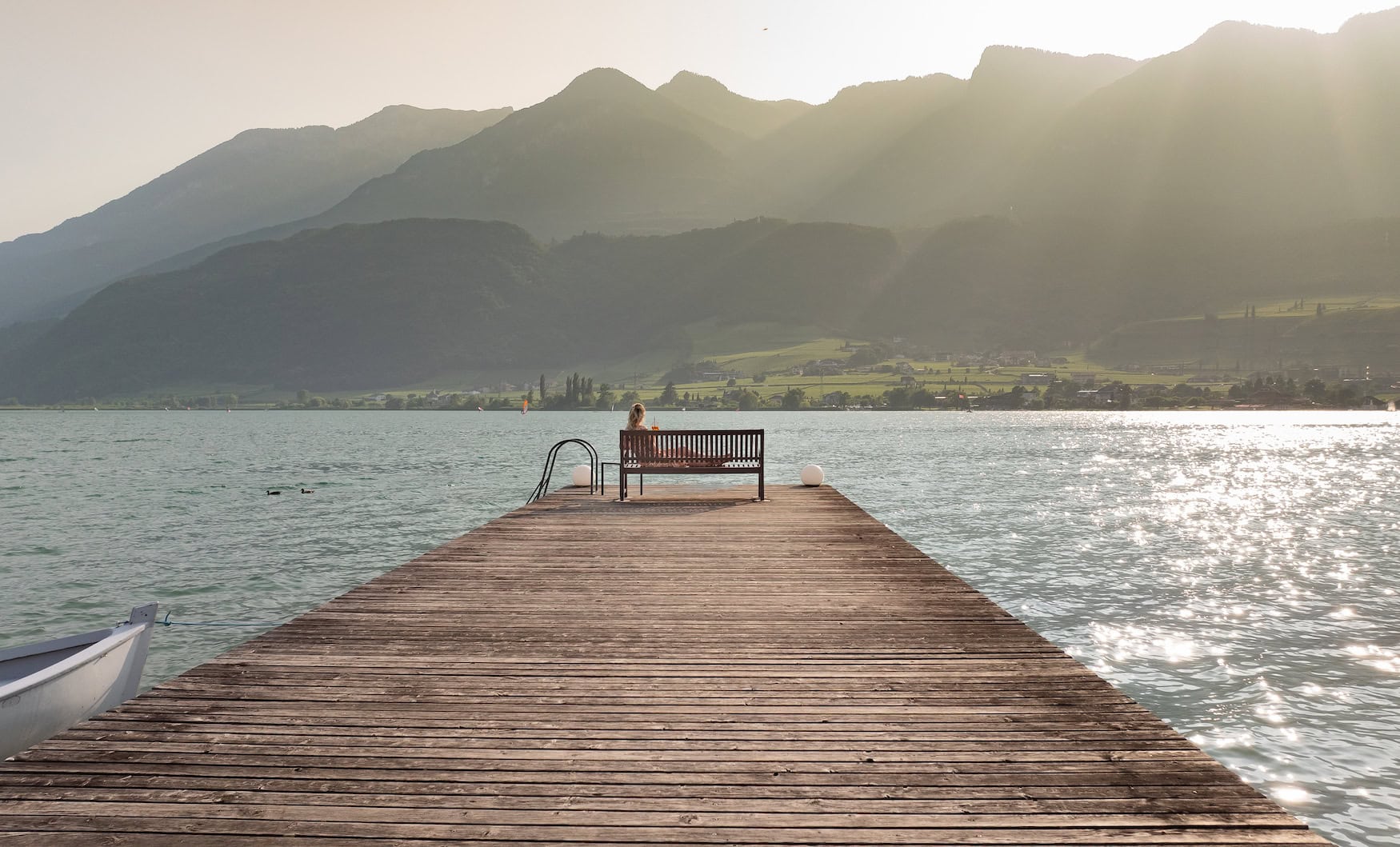 Holzsteg am Kalterer See mit Blick auf das Wasser und die umliegende Berglandschaft.