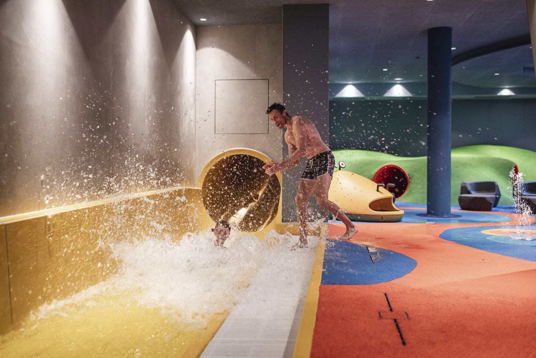 Kind auf der Indoor-Wasserrutsche im Falkensteiner Family Resort Lido mit einem Erwachsenen am Beckenrand.