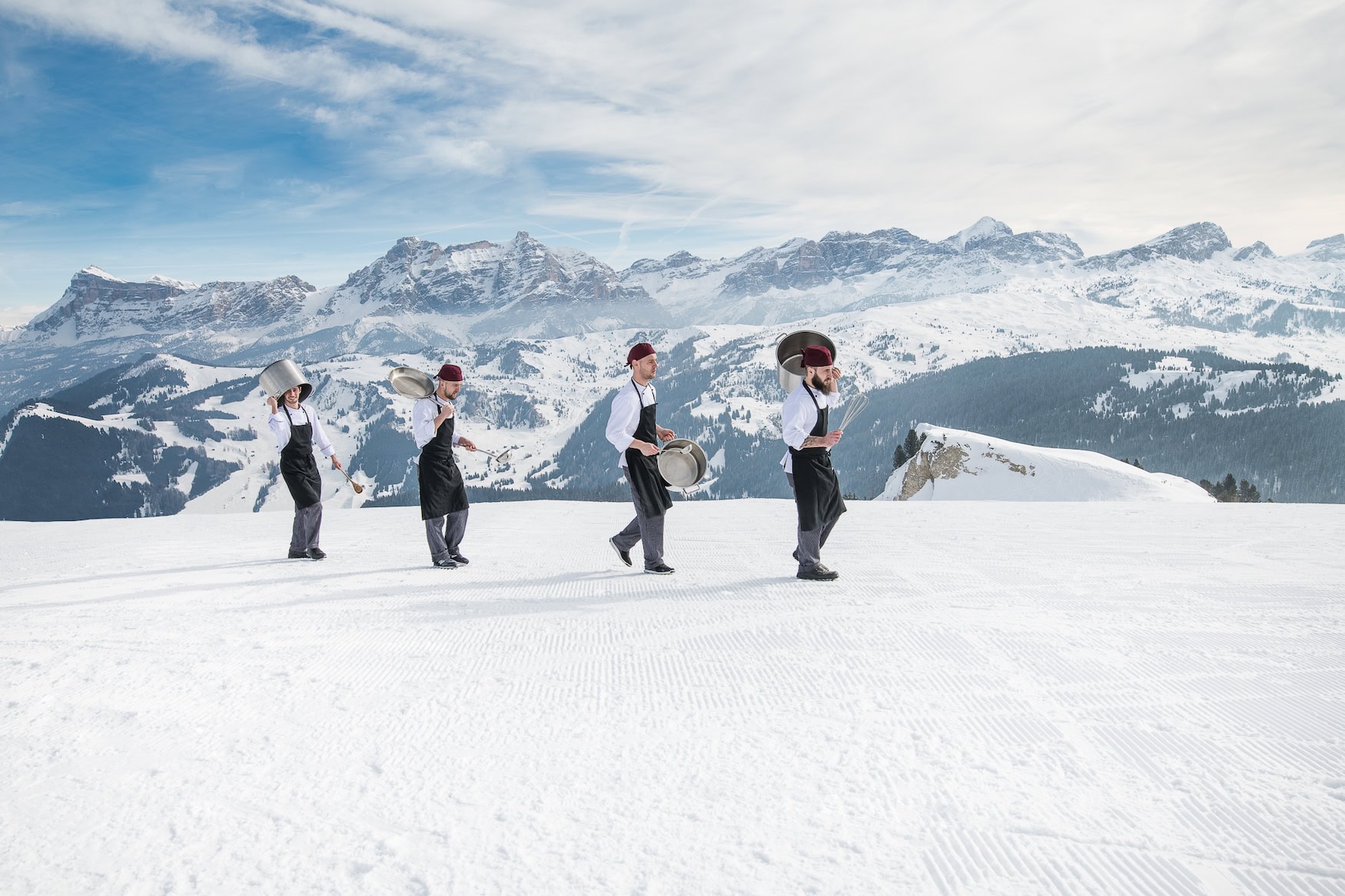 Köche laufen mit Kochtöpfen glücklich über eine Skipiste in Alta Badia in Südtirol