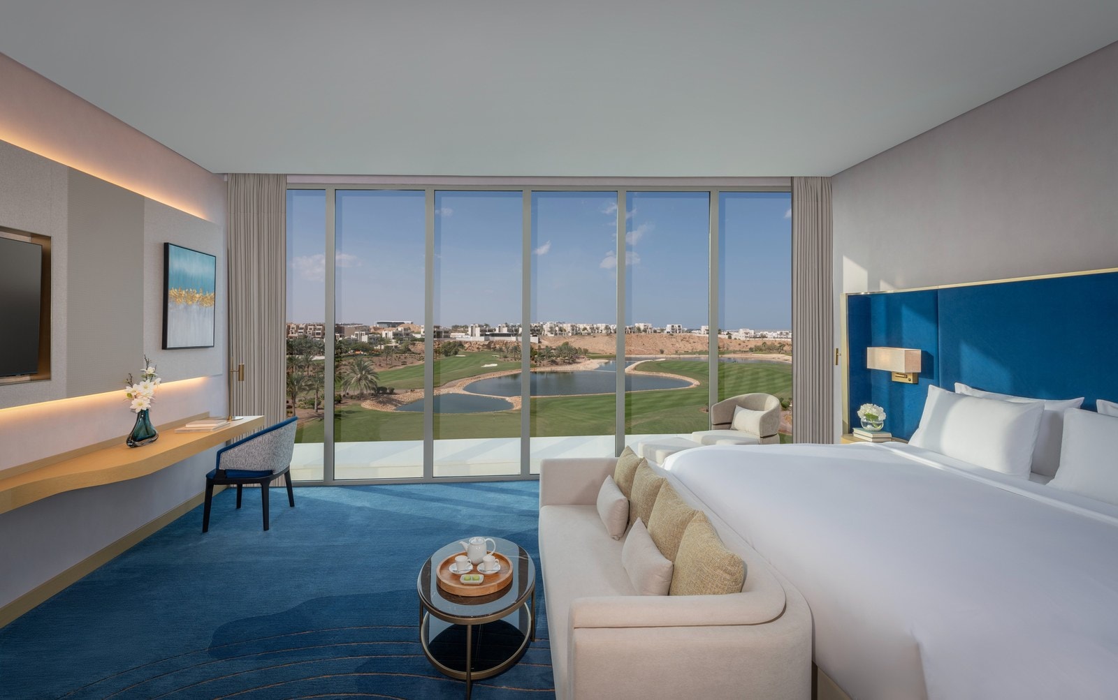 Junior Golf View Suite im Tivoli LA VIE Muscat mit blauem Kopfteil und raumhohen Fenstern zum Golfplatz mit Teichen und Palmen