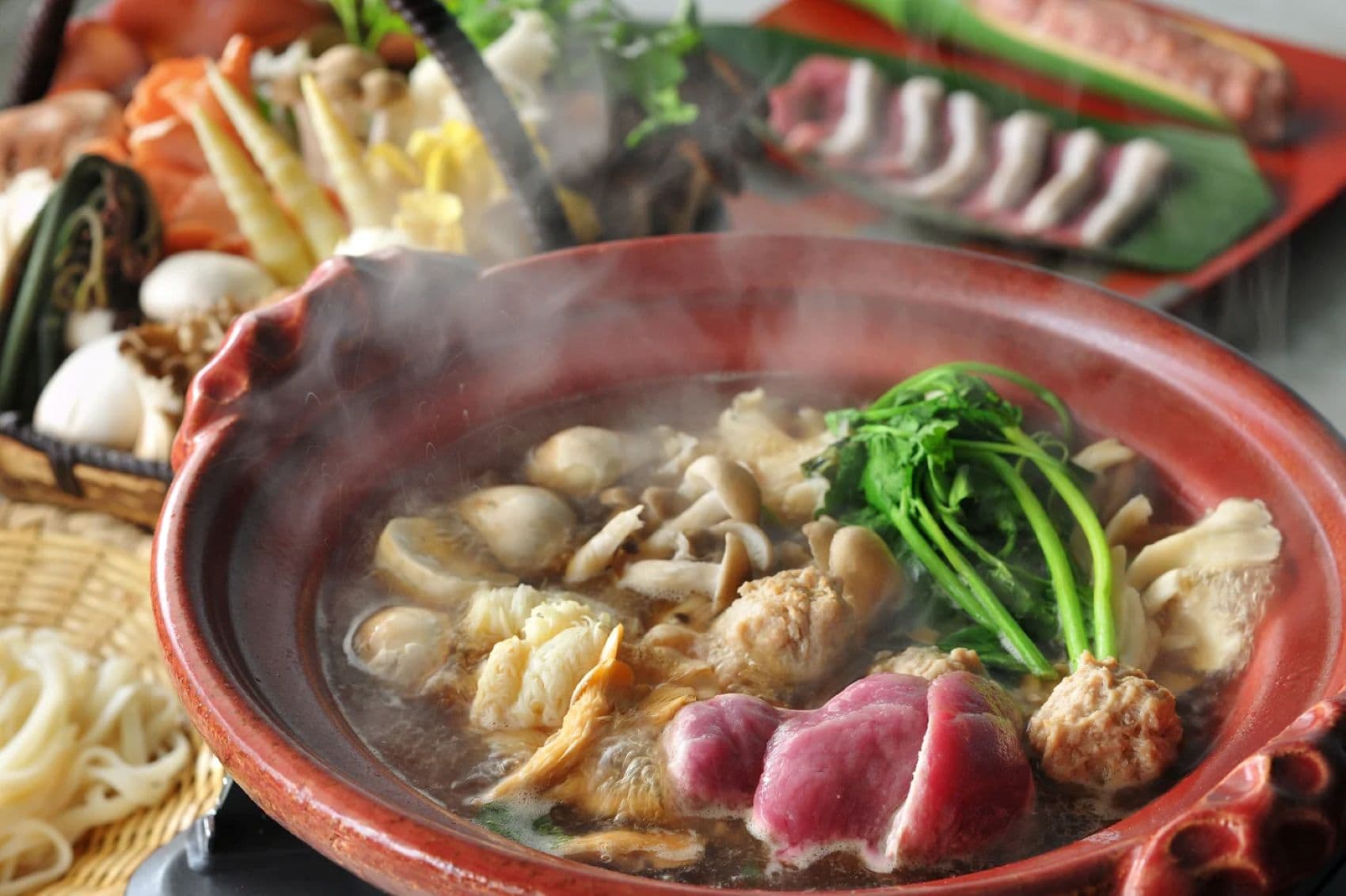 Japanischer Eintopf mit Pilzen, Gemüse und Fleisch in einer roten Keramikschale, serviert im KAI Zao
