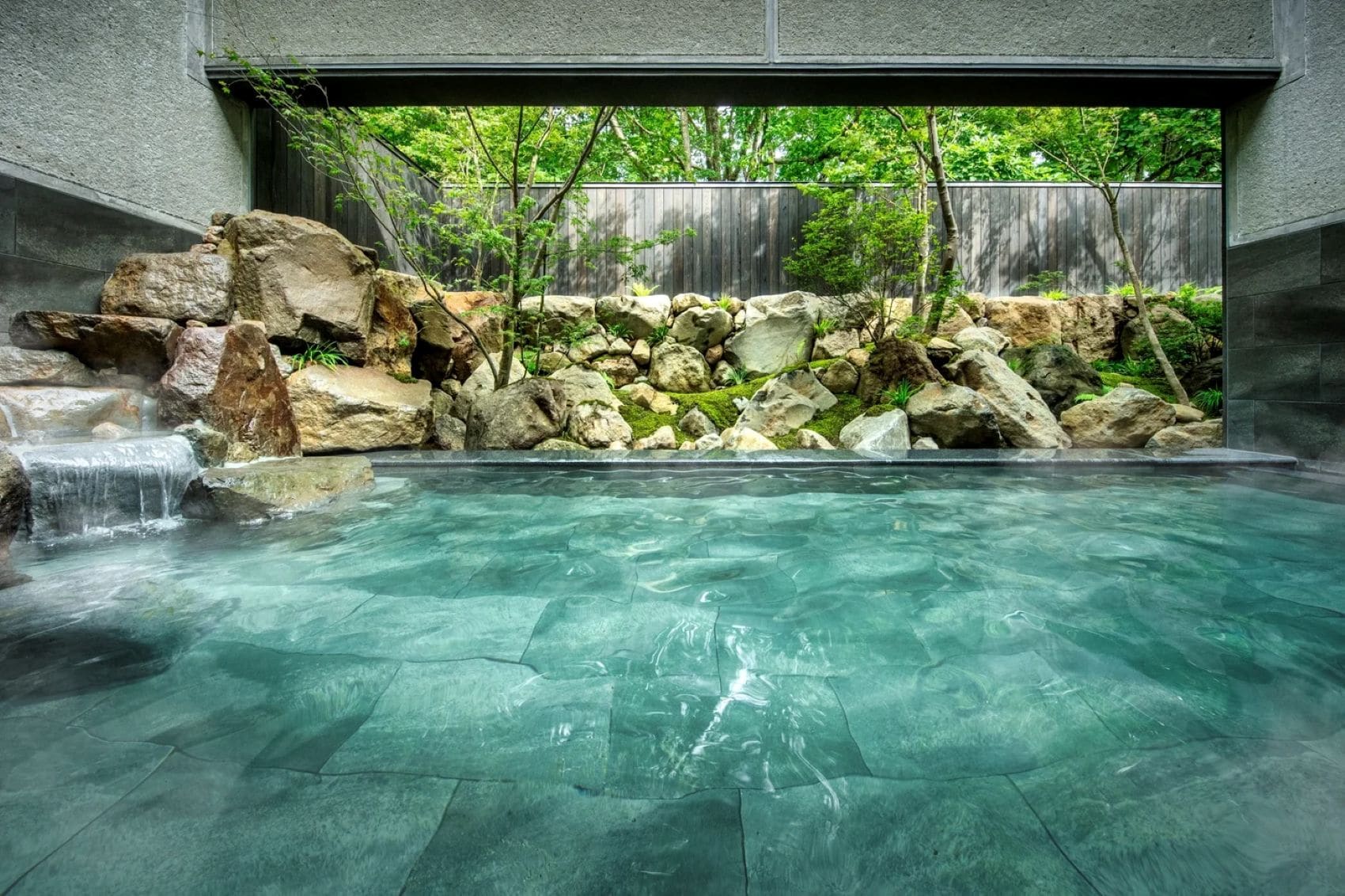 Thermalbecken im KAI Zao in Japan mit türkisfarbenem Wasser, natürlichen Felsen und Blick auf einen japanischen Garten