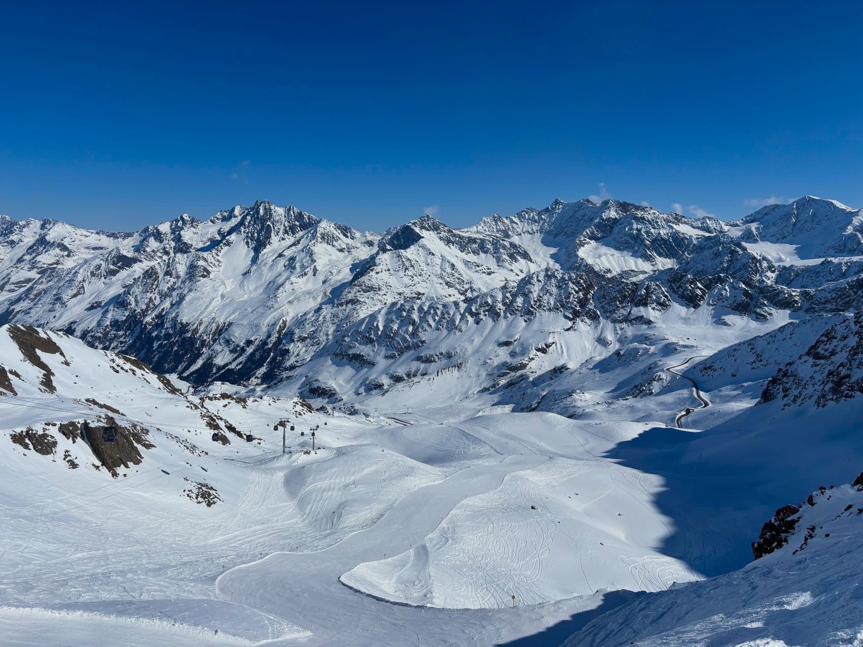 Panoramablick auf das Skigebiet Kaunertaler Gletscher in Tirol mit verschneiten Bergen, Skipisten und Liftanlagen unter blauem Himmel.