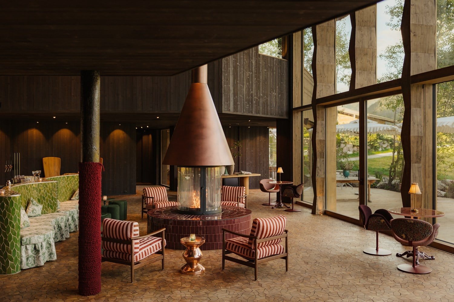 Lounge im Torhaus von LaPosch Living Lands mit Hängekamin, gestreiften Sesseln und raumhohen Fenstern zum Garten