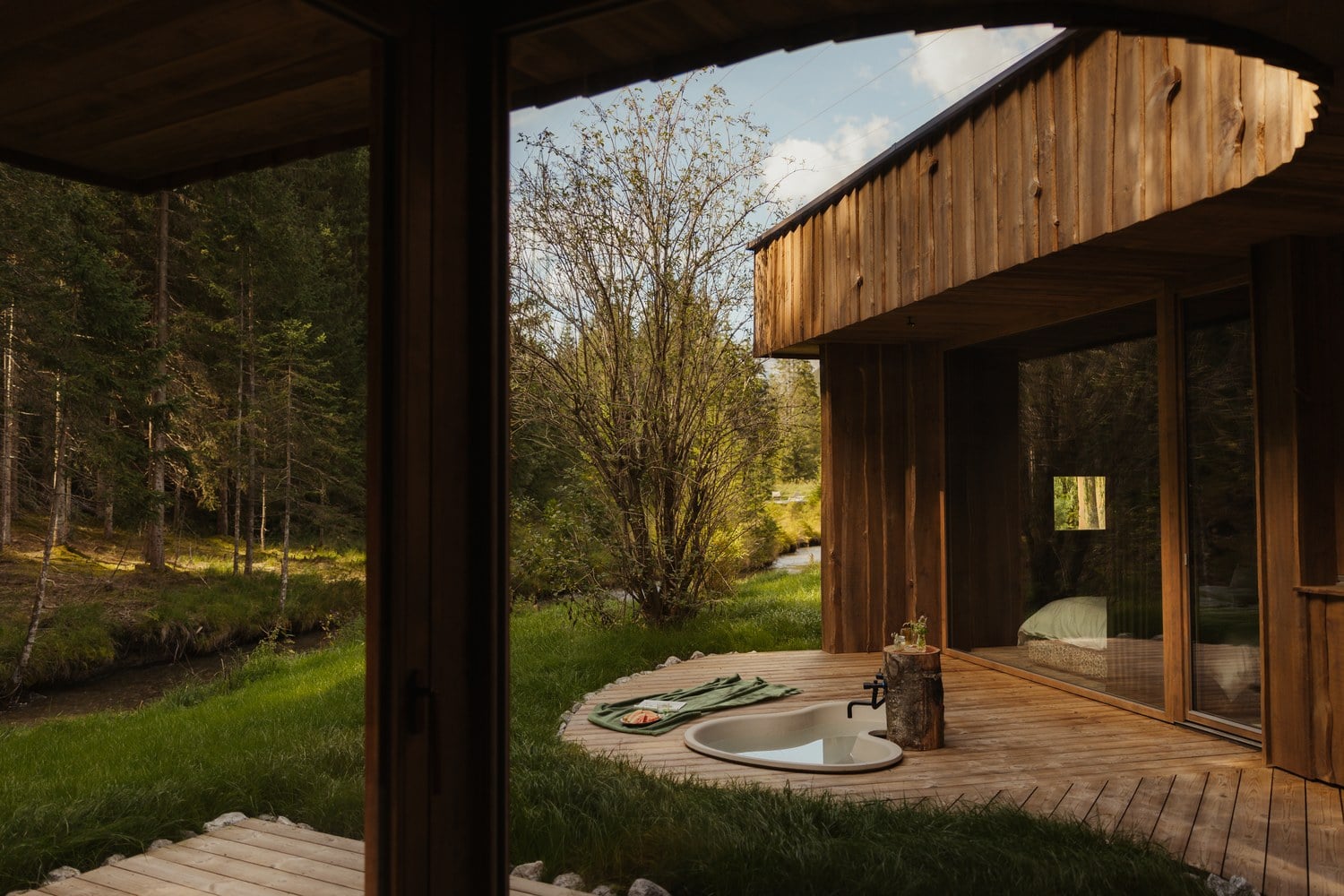 Terrasse einer Waldbach-Loge von LaPosch Living Lands mit Hot Pot, Wiese und Bachlauf