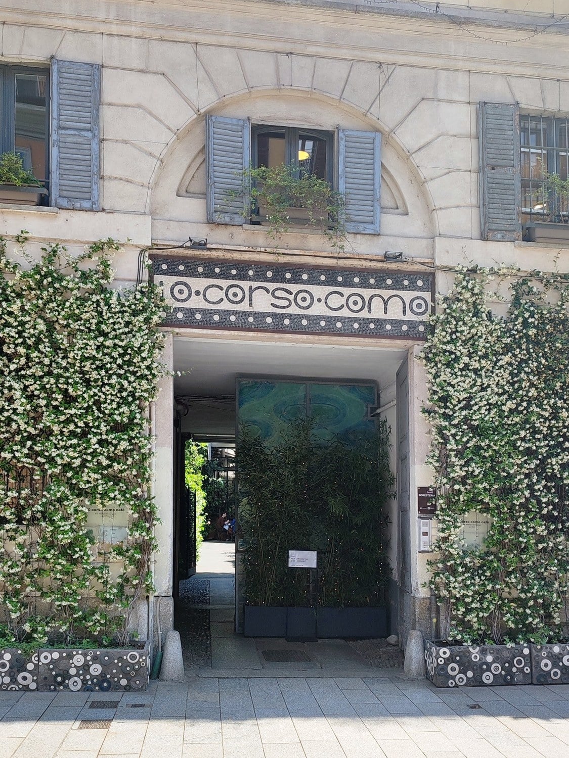 Eingang des Conceptstores 10 Corso Como in Mailand mit Mosaikschriftzug und blühendem Sternjasmin an der Fassade