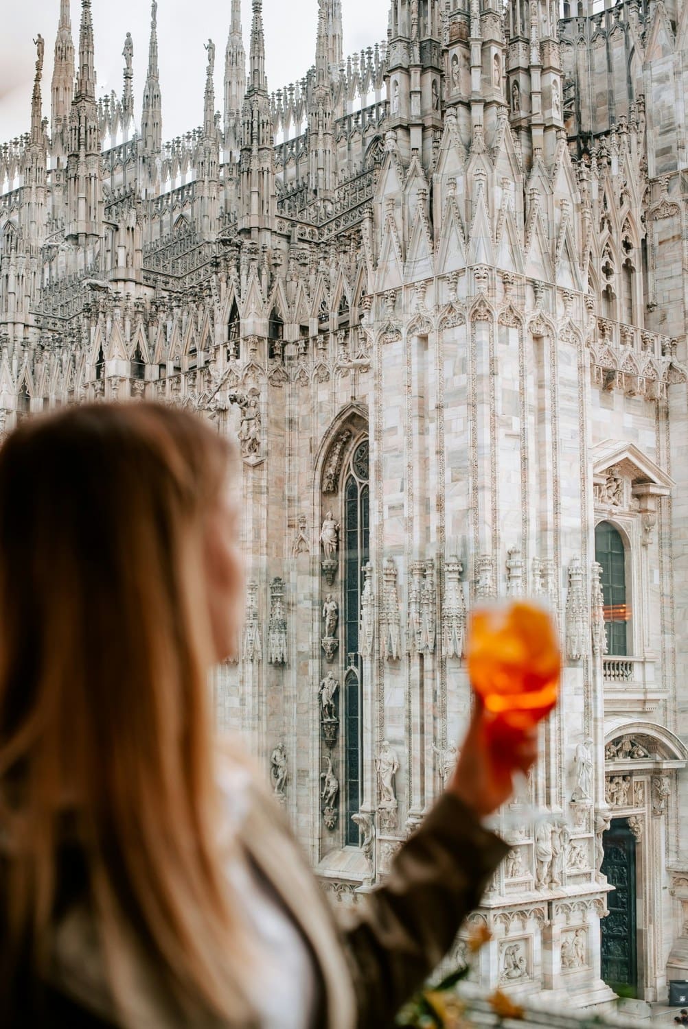 Frau mit Aperol Spritz vor den Marmorfialen des Mailänder Doms