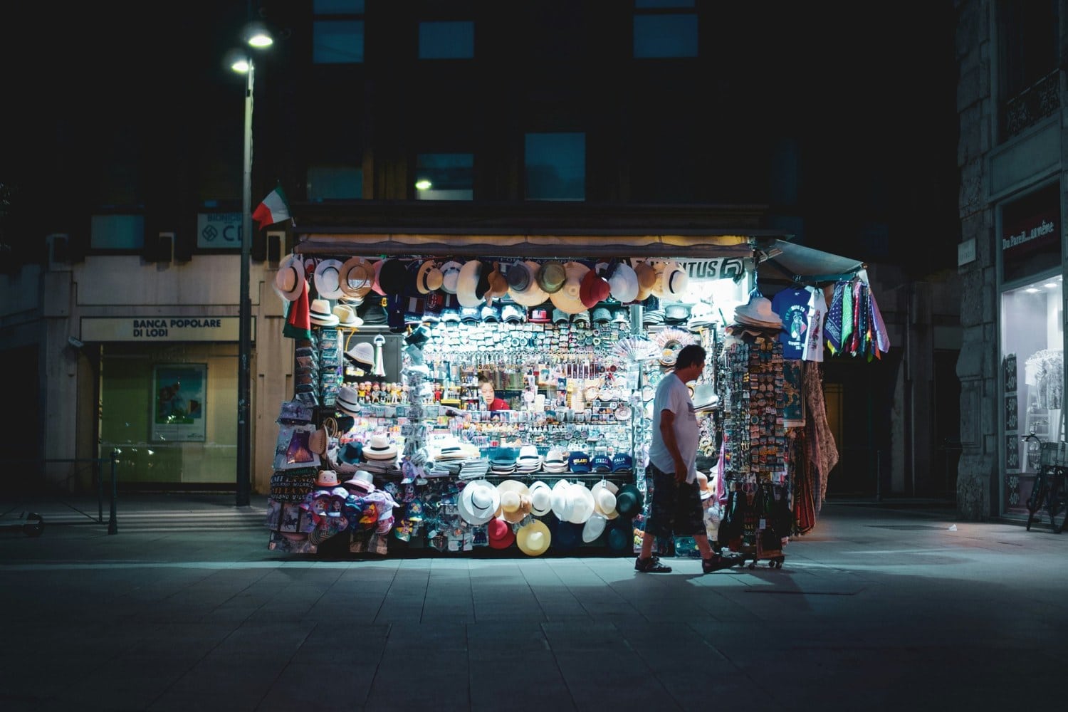 Hell erleuchteter Souvenirkiosk mit Hüten, Magneten und Fußballtrikots bei Nacht in Mailand