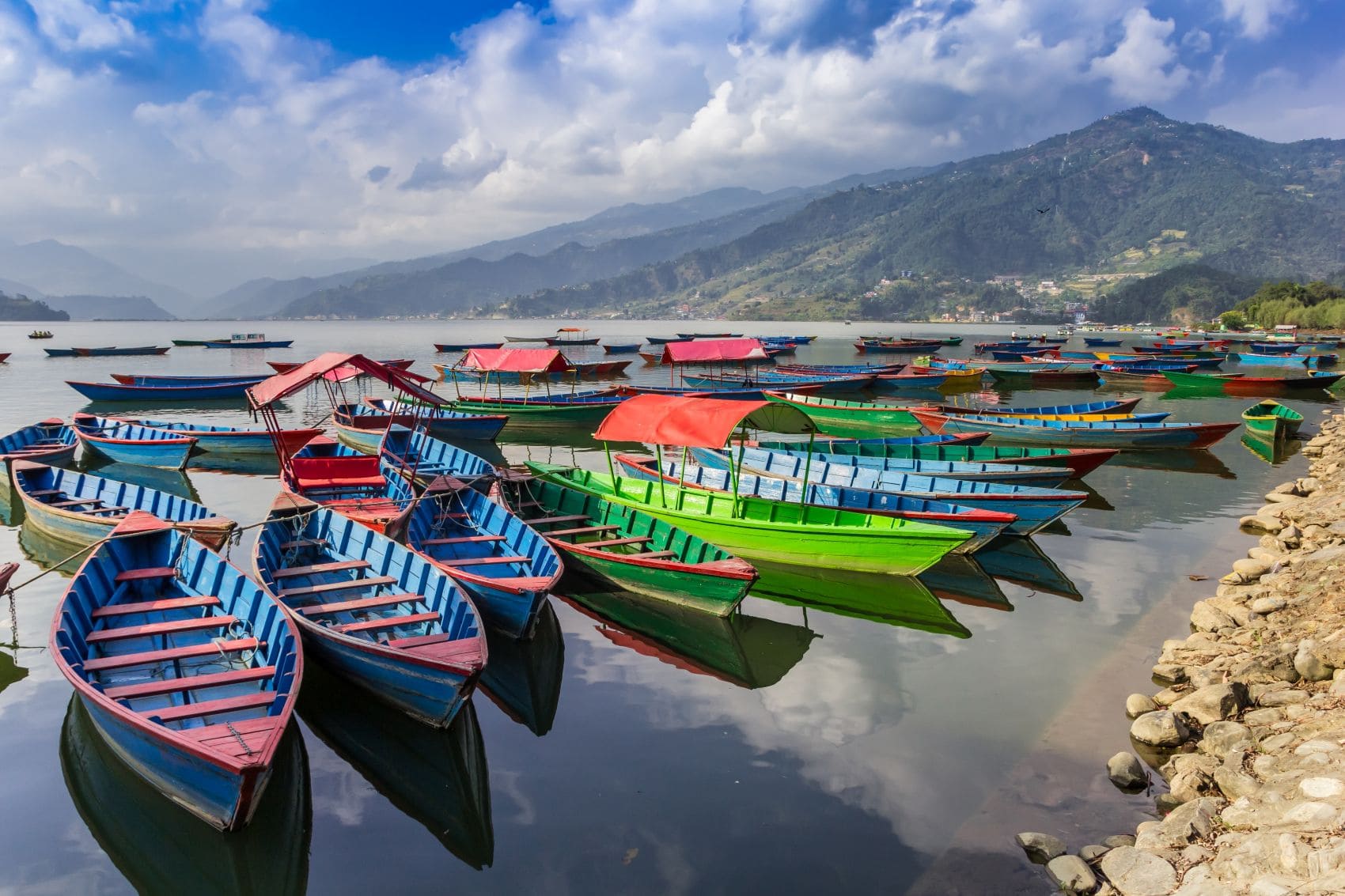 Bunte Holzboote auf dem Phewa-See in Pokhara, Nepal, vor einer Berglandschaft
