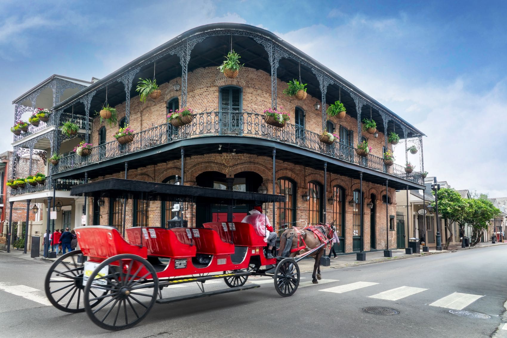 Historisches Backsteingebäude mit schmiedeeisernen Balkonen und roter Pferdekutsche im French Quarter von New Orleans.
