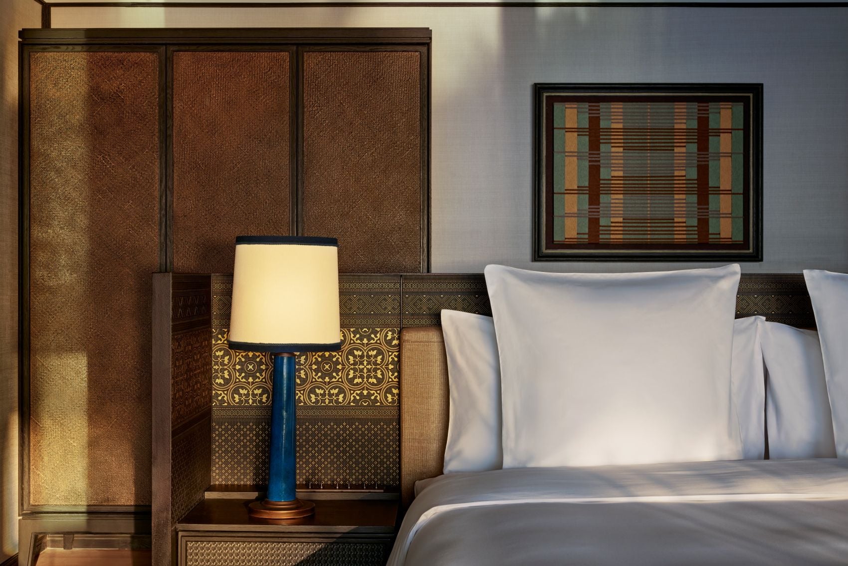 Schlafzimmer einer Beachfront Pool Villa im Park Hyatt Phu Quoc in Vietnam mit großem Bett, gemusterten Holzpaneelen, blauem Lampenfuß und dekorativem Wandbild.