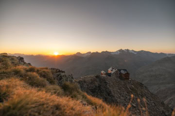 Das Ramolhaus auf einem felsigen Bergrücken im warmen Licht der tief stehenden Sonne, im Hintergrund Gipfel der Ötztaler Alpen mit Gletscherresten.