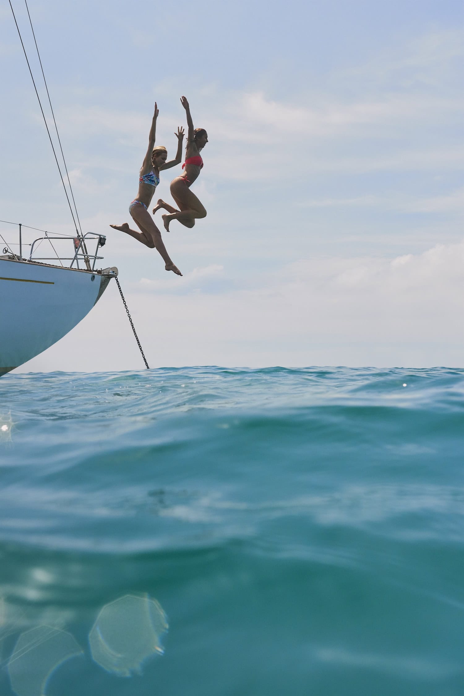zwei Frauen springen von einem Boot ins türkise Wasser