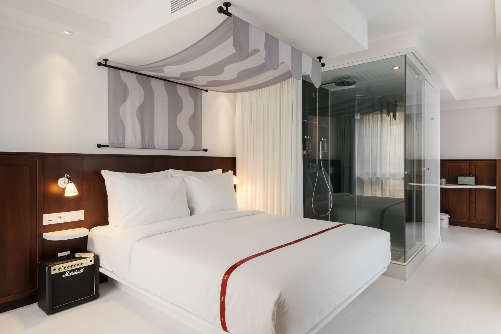 Helles Lovely-Doppelzimmer im Ruby Lilou Marseille mit großem Bett, dunkler Holzvertäfelung, gläserner Regendusche und Marshall-Verstärker.