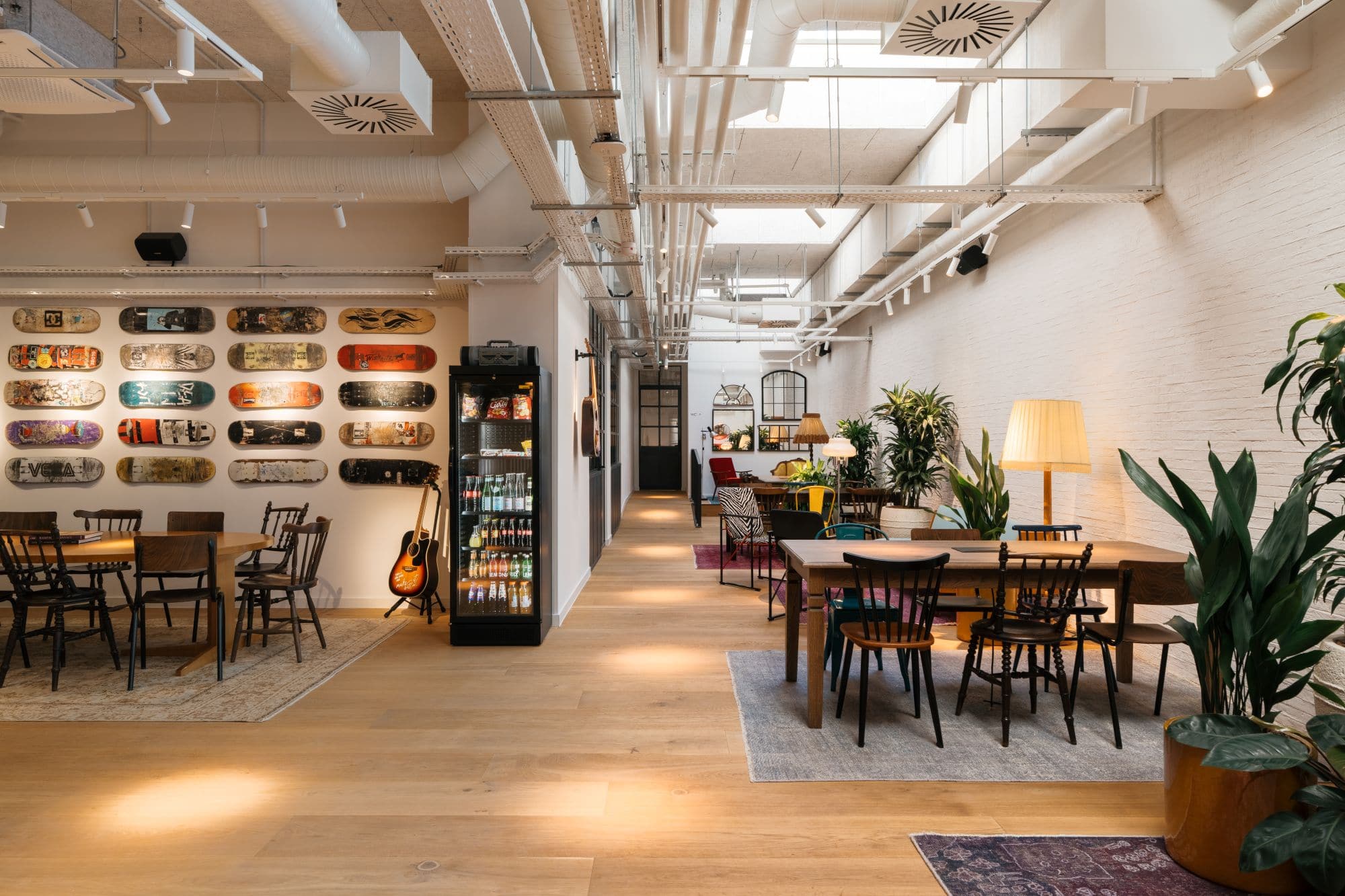 Coworking-Bereich Ruby Yani in Marseille mit Skateboards an der Wand, Holztischen, unterschiedlichen Stühlen und industriell gestalteter Decke.