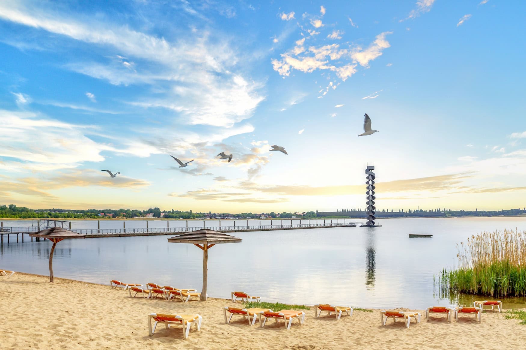 Ferien in Sachsen-Anhalt 2026: Sandstrand mit Liegestühlen und Sonnenschirmen am See bei Bitterfeld, darüber fliegende Möwen.