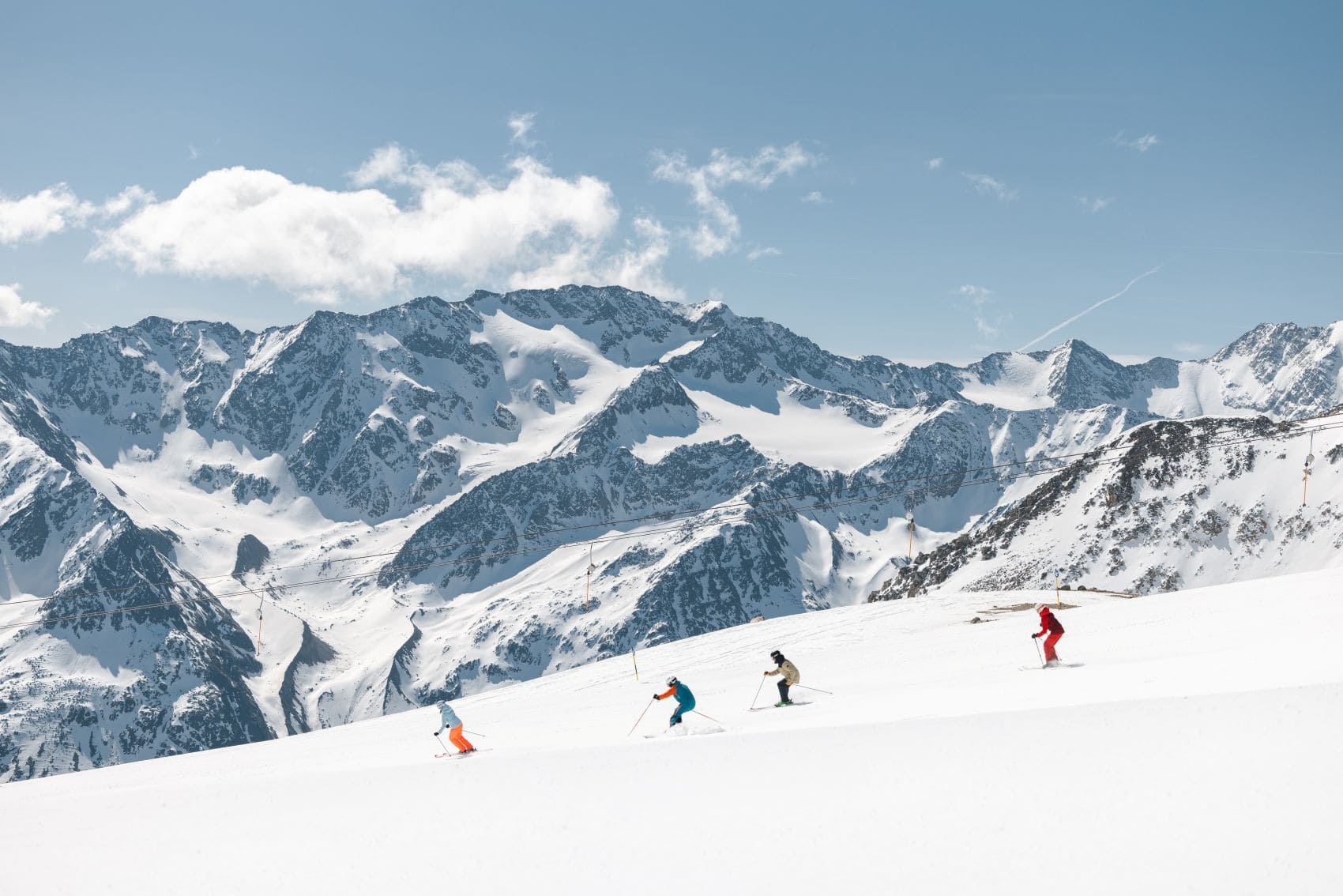 Vier Skifahrer fahren auf einer breiten, schneebedeckten Piste in Sölden in Tirol vor einem Panorama der Ötztaler Alpen.