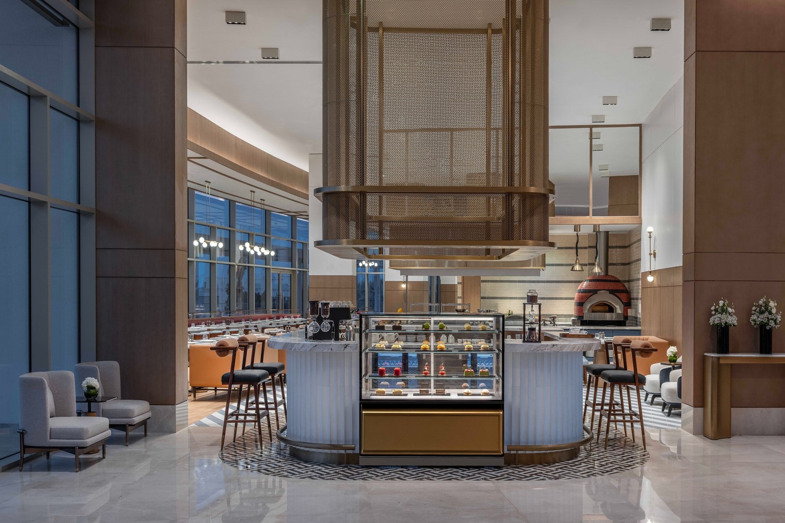 S O L É Lounge im Tivoli LA VIE Muscat mit Marmortresen, Patisserie-Vitrine und Messinggitter, dahinter das Restaurant mit Pizzaofen