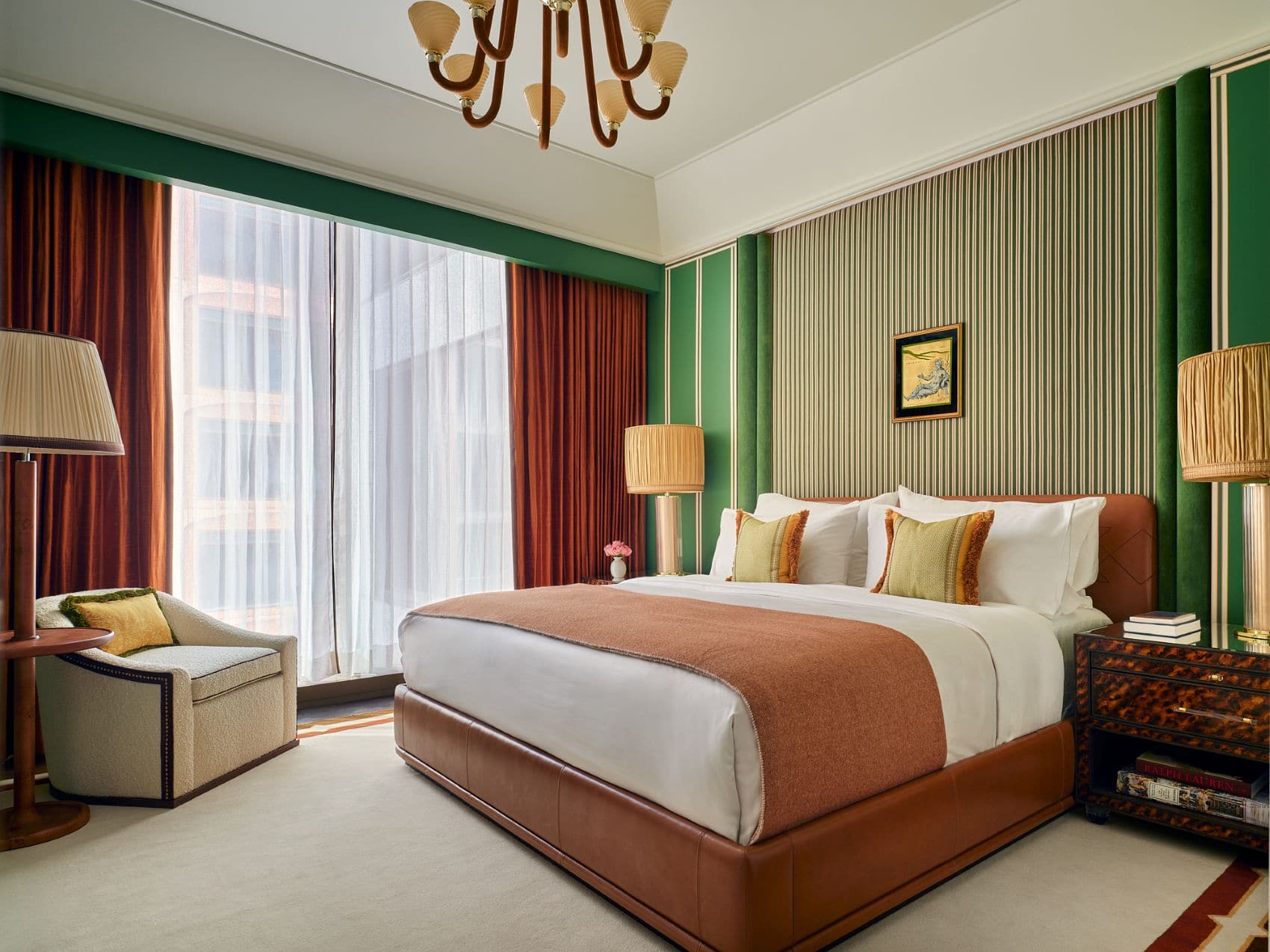 Schlafzimmer einer Suite im The Knox in Dallas mit grün gestreifter Wand, lederbezogenem Doppelbett, rostfarbenen Vorhängen und dekorativen Nachttischen.