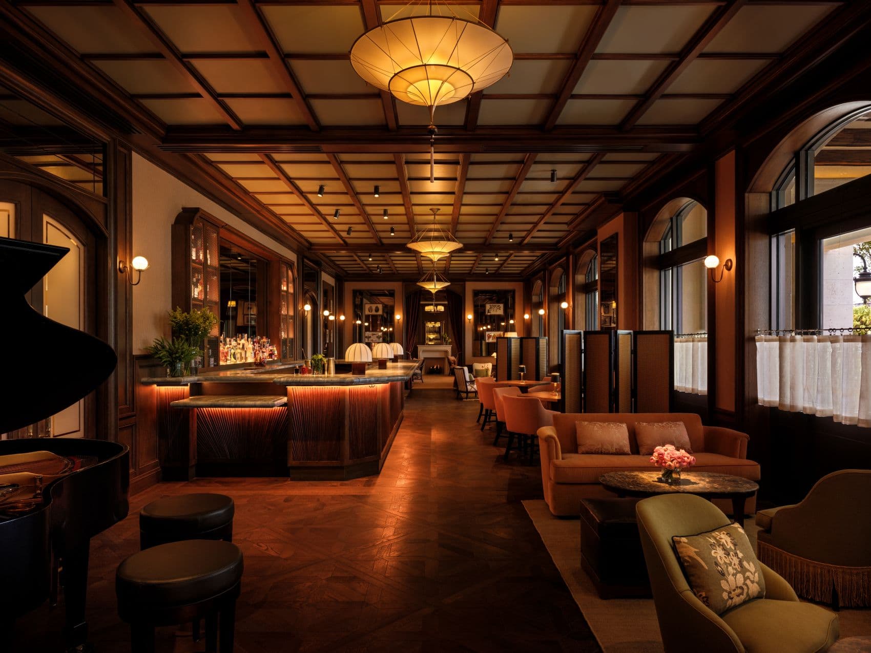 Jack’s Bar im The Nora Hotel in West Palm Beach mit dunkler Holzvertäfelung, beleuchteter Bartheke, Kassettendecke, Flügel und gemütlichen Sitzgruppen.