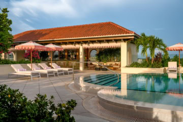 Dachterrasse Lilly’s Rooftop im The Nora Hotel in West Palm Beach mit Swimmingpool, rosafarbenen Sonnenschirmen, Sonnenliegen, Palmen und überdachter Bar.