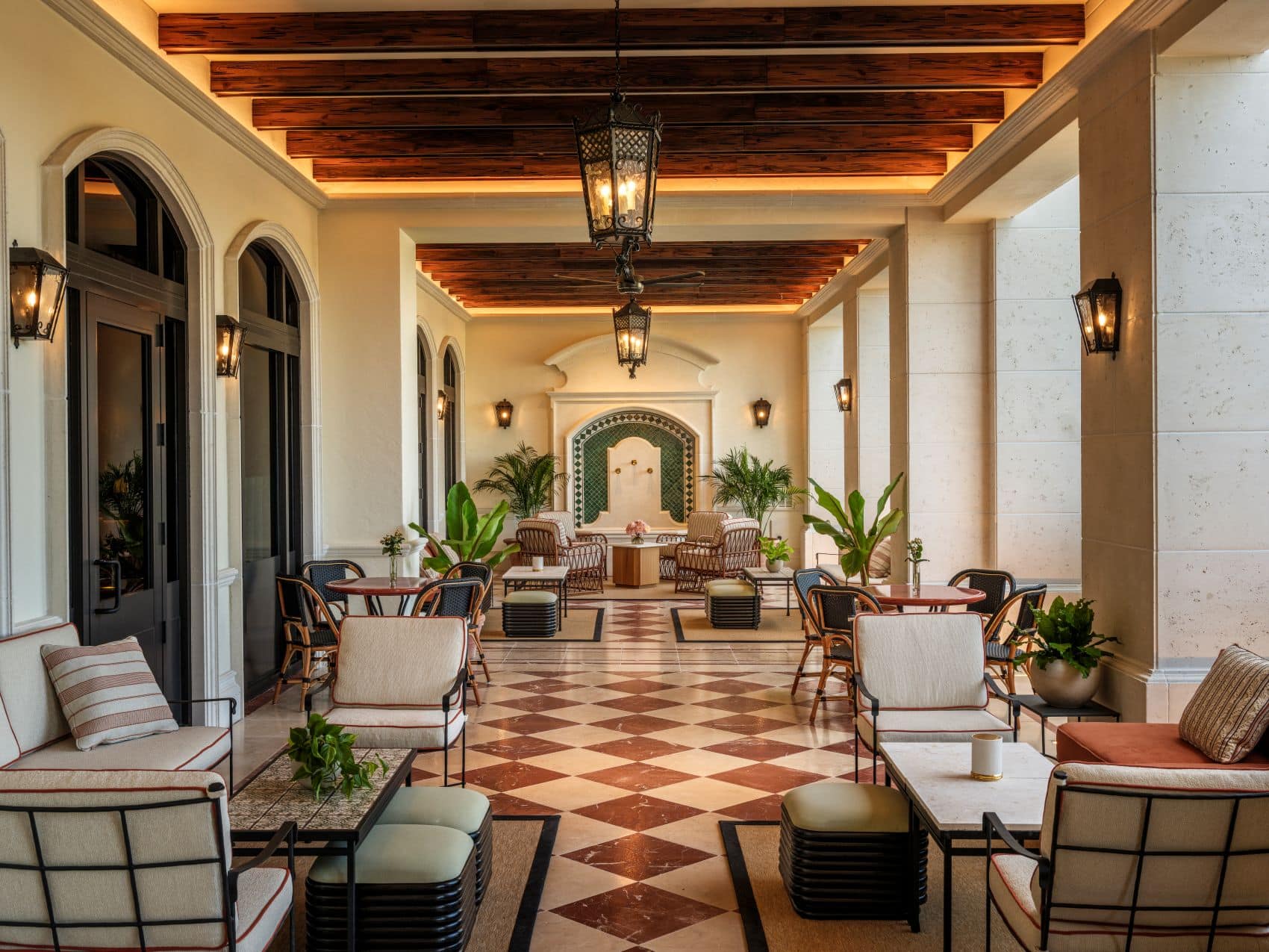 Überdachte Loggia im The Nora Hotel in West Palm Beach mit rot-weiß kariertem Steinboden, dunklen Holzbalken, Rundbögen und eleganten Sitzgruppen.