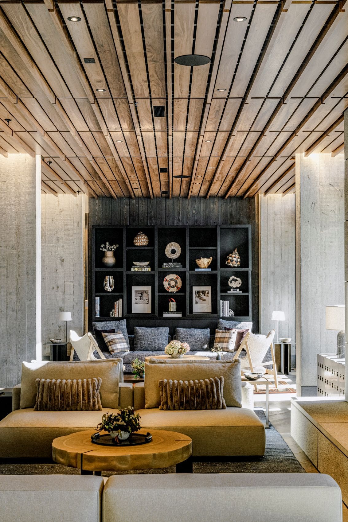 Lobby des The Observatory, A Viceroy Resort, in Idaho mit hellen Sofas, Holztischen, dunkler Regalwand und einer Decke aus versetzt angeordneten Holzlamellen.