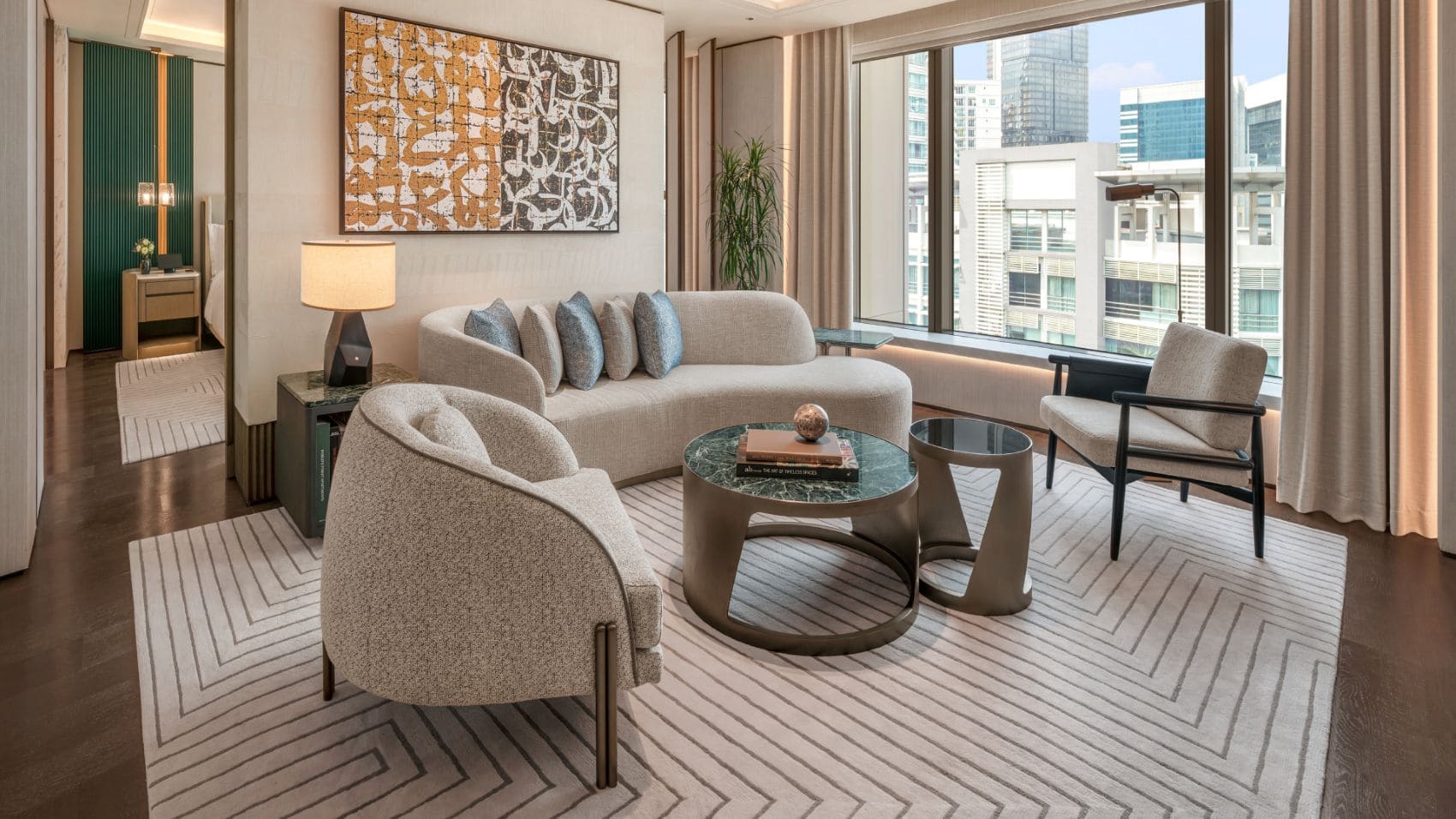 Wohnbereich einer Signature Suite im Waldorf Astoria Kuala Lumpur mit geschwungenem Sofa, Sesseln, abstraktem Kunstwerk und großen Fenstern.