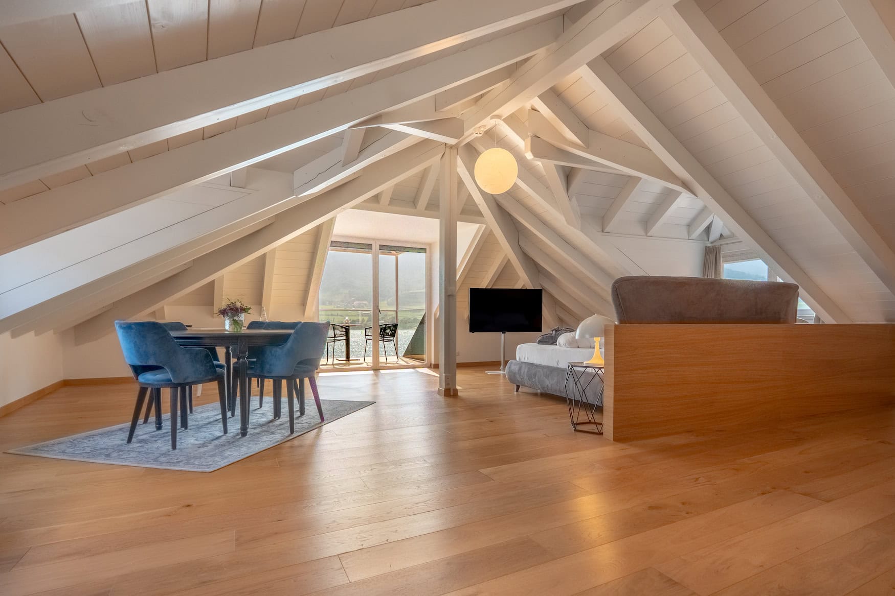 Helle Suite im Parc Hotel am See mit Holzboden, offenem Dachstuhl, Sitzbereich und großen Fenstern.